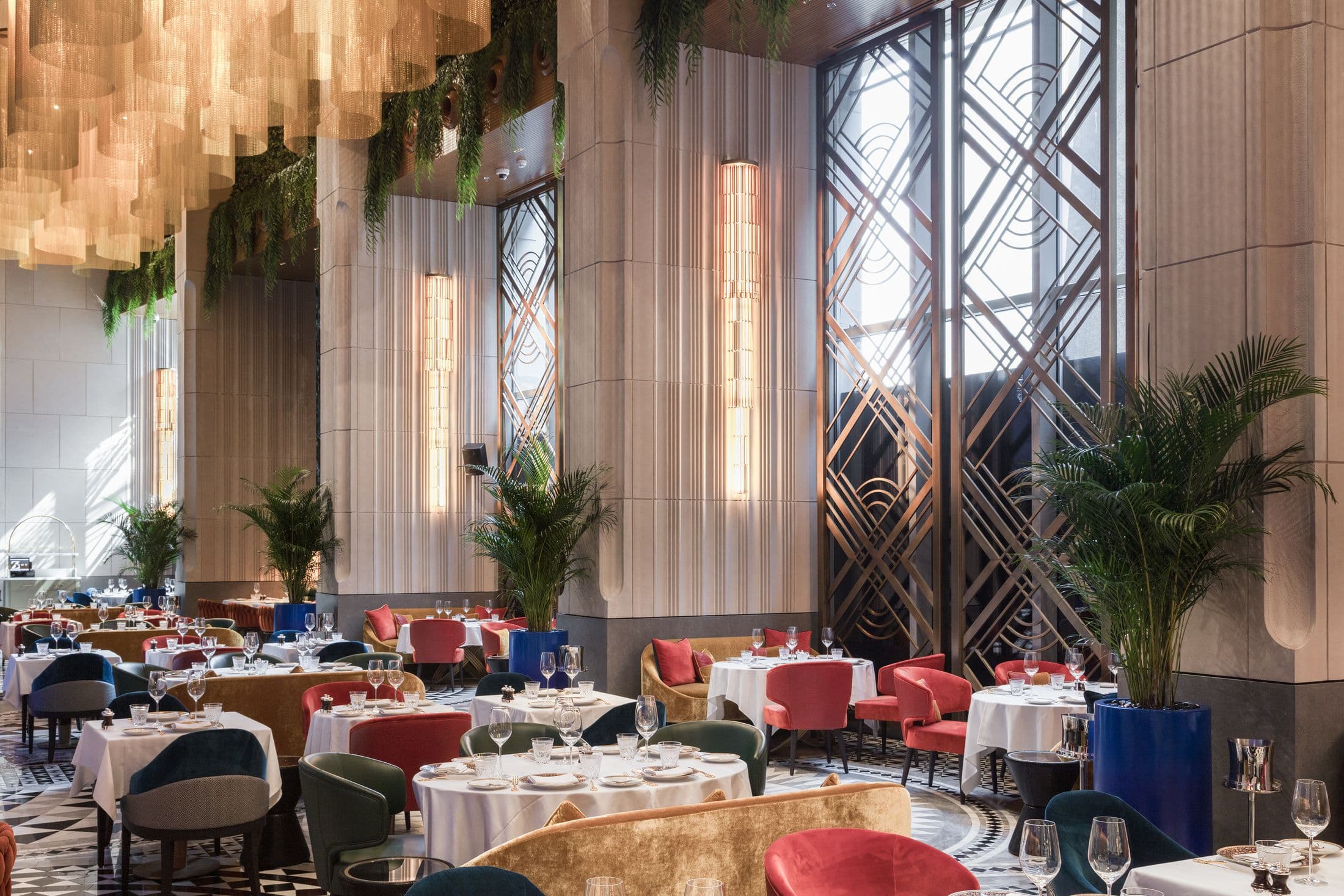 The main dining room at ZENON by day, tables laid under a gold chain chandelier beside a tall Art Deco window